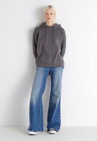 Grå hettegenser med snorer, kombinert med lyseblå vide jeans. Antrekket har en avslappet passform og enkelt design.