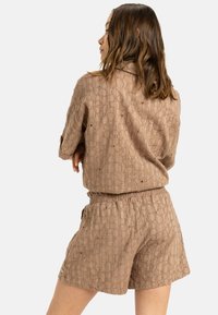 Tan textured tvådelad outfit med en lös passform skjorta med krage och shorts med elastisk midja, båda med ett cirkulärt mönster.