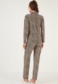 Set pidžame s leopard uzorkom, dugih rukava i hlača, izrađen od mekanog materijala, s detaljem na dugmetu i opuštenim krojem. Svijetlo bež i smeđi tonovi.