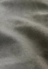 Tissu gris doux avec une texture lisse et veloutée, présentant des vagues et des plis subtils. La couleur est uniforme avec un éclat discret et mat.