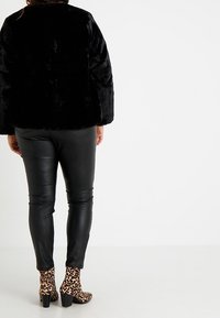 Schwarze Kunstfelljacke, figurbetonte schwarze Lederhosen und Ankle Boots mit Leopardenmuster. Rückansicht; weiche Textur, moderner Schnitt.