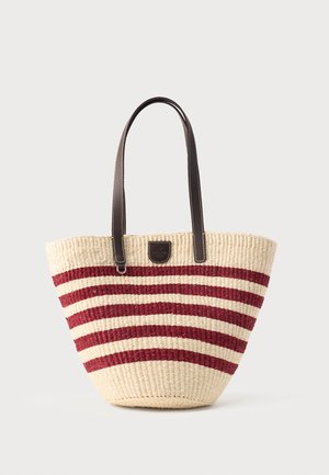 Woven straw tote bag with horizontal red and natural stripes, featuring two dark brown leather handles and a small leather patch on the front.