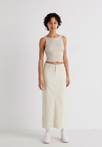 Beige kort tanktop og lang, kremhvit denimskjørt med glidelås foran. Brukt med hvite sneakers, satt mot en enkel bakgrunn.