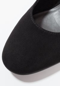 Chaussure en daim noir avec un bout arrondi et un intérieur lisse. Détails de couture le long du bord supérieur. Semelle plate et flexible visible en bas.