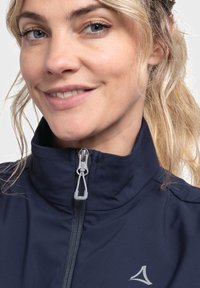 Marineblaue Jacke mit hohem Kragen und grauen Reißverschlussdetails. Verfügt über ein kleines Logo auf der linken Seite und besteht aus weichem, glattem Material.