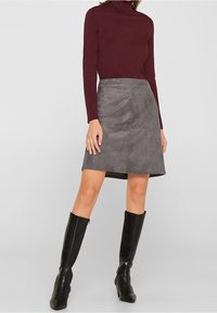 Jupe en daim gris à coupe droite avec des détails de couture à l'avant, associée à un haut bordeaux à manches longues et des bottes noires jusqu'aux genoux.