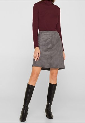 Jupe en daim gris à coupe droite avec des détails de couture à l'avant, associée à un haut bordeaux à manches longues et des bottes noires jusqu'aux genoux.