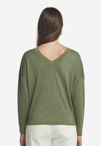 Grön V-halsad tröja med långa ärmar, mjuk textur och avslappnad passform. Justerbar ribbad nederkant och manschetter för en bekväm look.