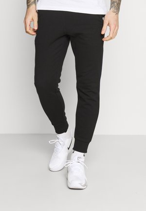 Osoba nosząca czarne spodnie dresowe, białe skarpetki za kostkę oraz białe buty sportowe z czarnymi logo Nike swoosh.