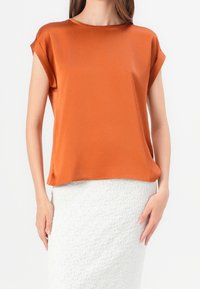 Halenka s krátkým rukávem v barvě spálené oranžové z saténové tkaniny s kulatým výstřihem a volným střihem, kombinovaná s texturovanou bílou sukní.