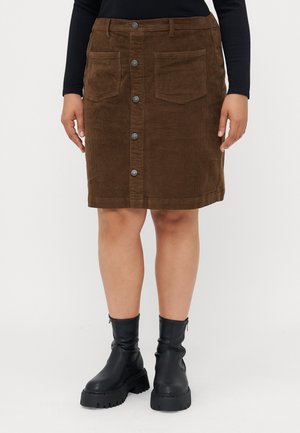 Jupe en velours côtelé marron à boutons sur le devant avec deux poches avant, portée avec des bottines noires épaisses et un haut noir à manches longues.