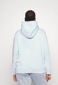 Sudadera azul claro con un ajuste relajado, textura suave y una capucha grande y ajustable. Presenta puños y dobladillo acanalados, vista desde la parte de atrás.