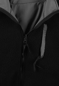 Czarna bluza polarowa na zamek z fakturowaną zewnętrzną warstwą i gładkim podszyciem. Zamek w kontrastowym kolorze oraz branding na zapince suwaka.