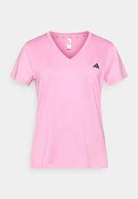 Tričko s krátkym rukávom a výstrihom do V v svetlo ružovej látke. Naľavo na hrudi je čierne logo Adidas a materiál má hladkú textúru.