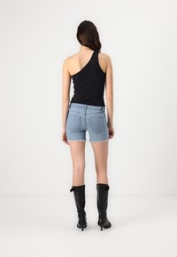 Čierny top na jedno rameno spárovaný s svetlomodrými denimovými šortkami so strapcami. Model nosí čierne topánky po kolená.