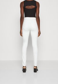 Jeans blancos ajustados de talle alto con dos bolsillos traseros, combinados con un body negro ajustado que presenta un detalle con corte en la espalda.