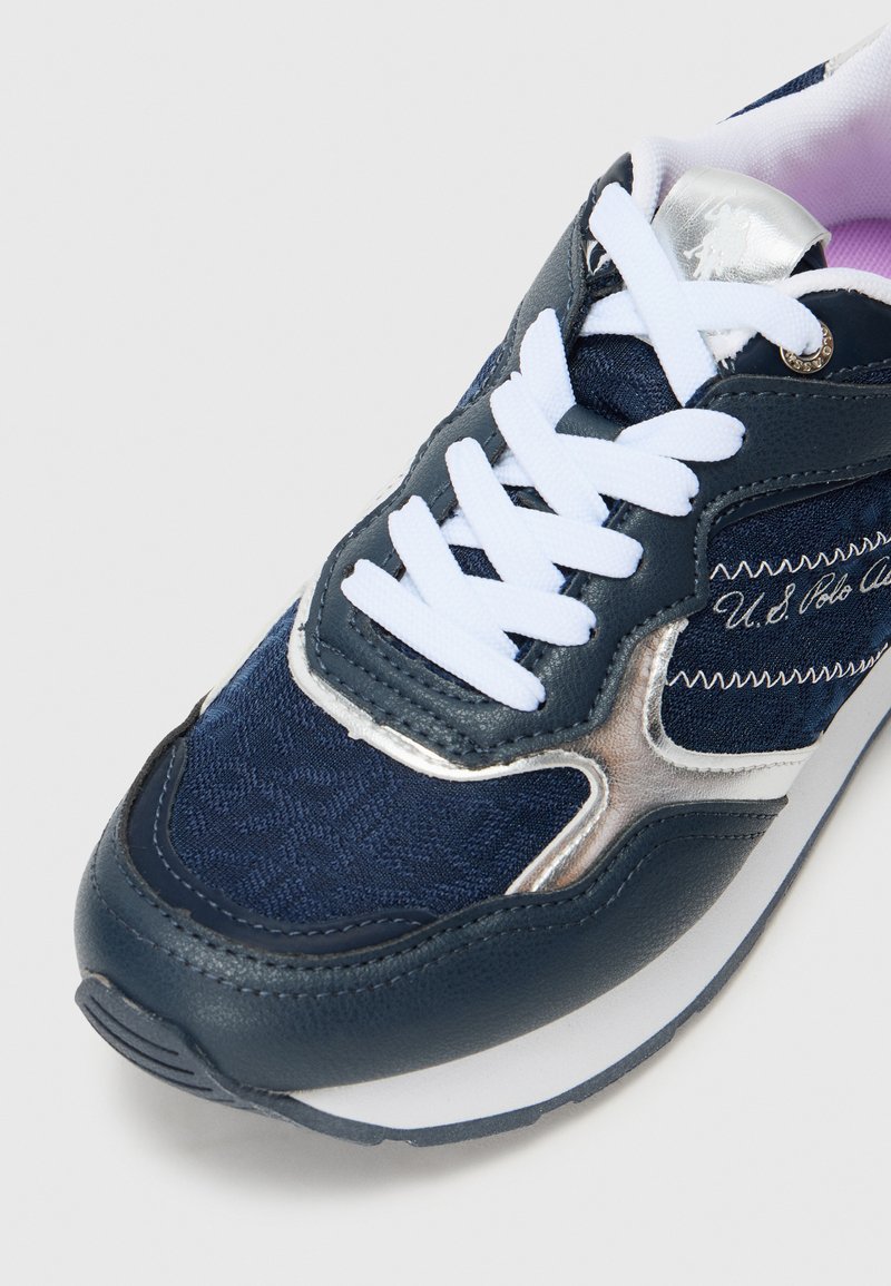 Baskets de sport bleu marine avec des lacets blancs, tige en cuir et textile, accents argentés, motif texturé et semelle intermédiaire blanche rembourrée.