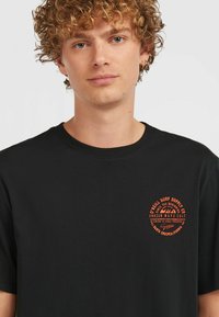 Black cotton t-shirt with short sleeves, featuring an orange circular logo on the left chest with text and wave graphics.