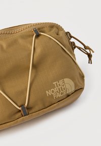 Καφέ συμπαγής θήκη με φερμουάρ και ελαστικό κορδόνι, με το λογότυπο "The North Face" σε υφασμάτινη, υφή.
