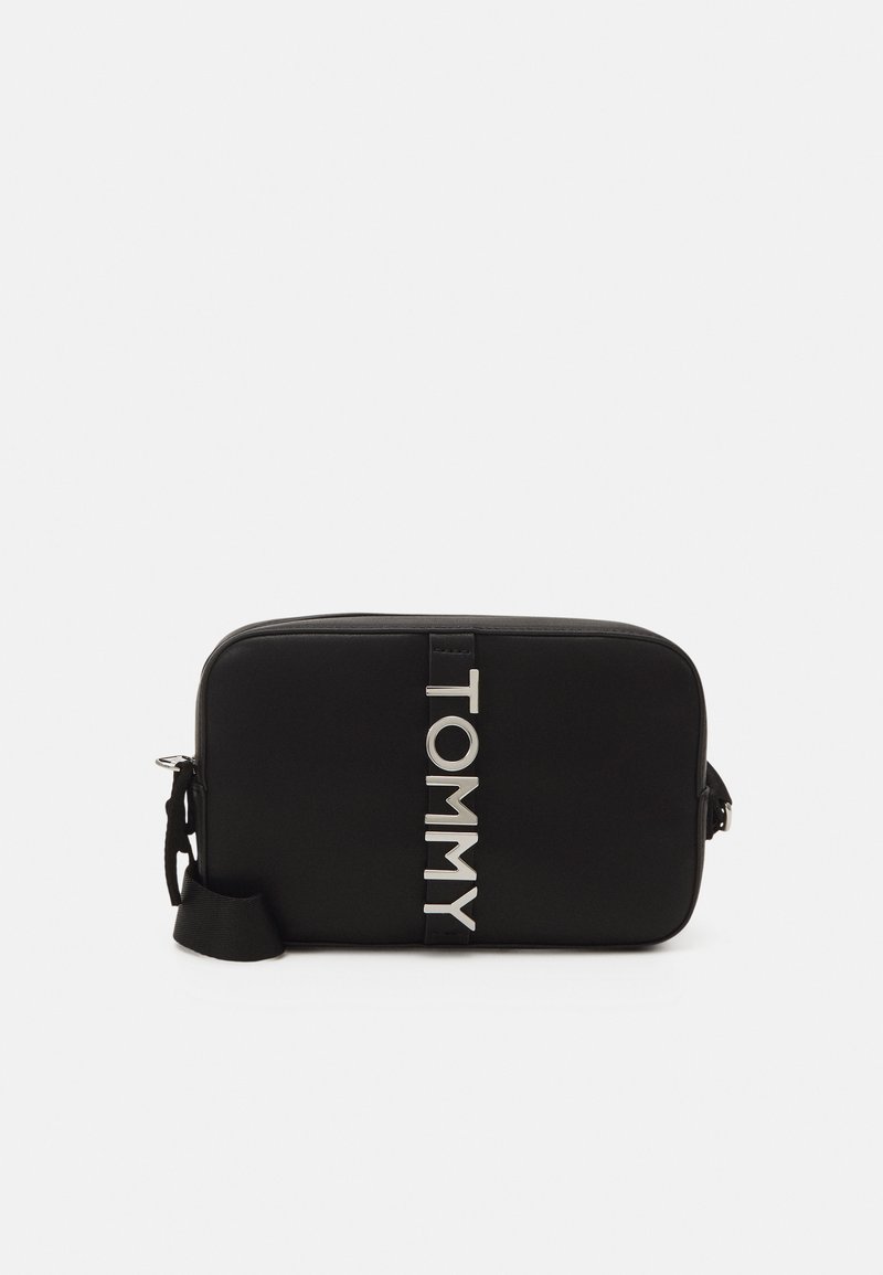Borsa rettangolare nera realizzata in materiale liscia, con un prominente logo argentato "TOMMY", una tracolla regolabile e chiusura con zip.