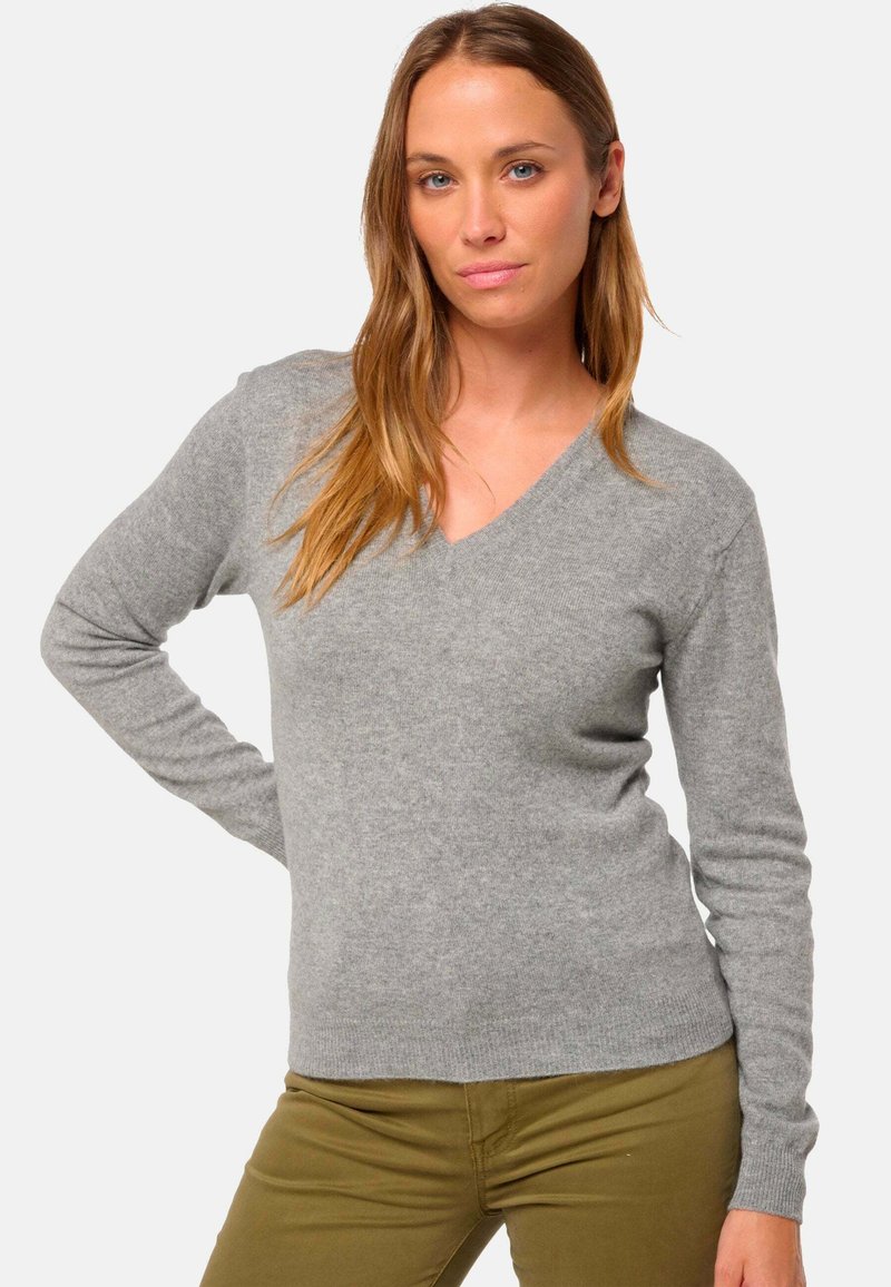 Pull gris à manches longues en V, fabriqué dans un matériau doux, porté avec un pantalon vert olive. Présente un design ajusté et des poignets côtelés.