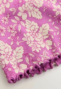 Lila bordázott textil, krémszínű virágmintával. Az alsó él fodros szegéllyel díszített, amely textúrát ad a dizájnnak.