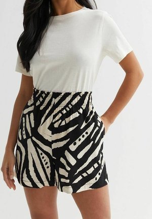 Femme portant un haut blanc uni à manches courtes associé à un short taille haute à motifs noir et blanc avec poches.