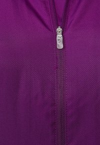 Lila zip-up jacka tillverkad av texturerat tyg, med en central silverfärgad dragkedja med varumärke och ett rutmönster över materialet.