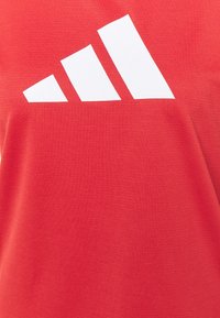 Camiseta roja hecha de tejido texturizado, con un gran logo blanco de tres rayas en la parte superior izquierda.
