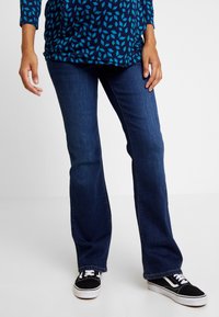 Mörkblå utsvängda jeans med en slät denimtextur, som bärs med svarta och vita sneakers. Toppens design har ett mönster med blå och marinblå nyanser.