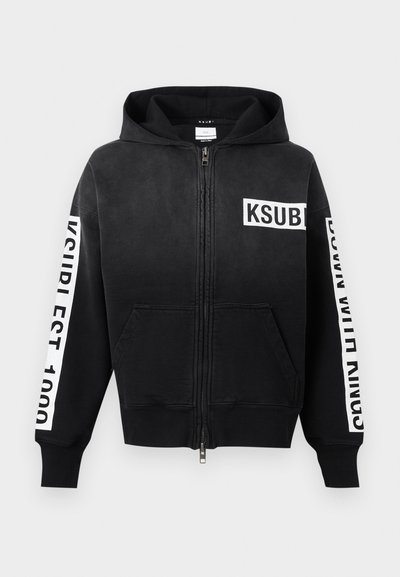 Μαύρη ζακέτα με φερμουάρ, εμπρός τσέπες, λευκό λογότυπο "KSUBI" στο στήθος και λευκές ρίγες κειμένου σε κάθε μανίκι.