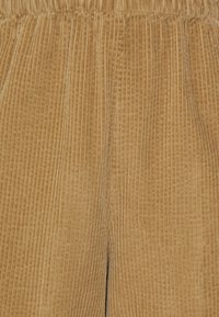 Kanvasbyxor i en varm tan-färg, med vertikal ribbat textur, ett elastiskt midjeband och rak ben-design.