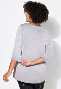 Haut gris ample à manches trois-quarts, encolure ronde, texture douce et ourlet arrondi. Présente un éclat subtil et un tissu lisse.