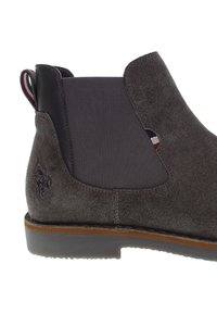 Stivaletto in suede grigio con pannelli elastici laterali e suola in gomma. Presenta un logo impresso sul tallone e una linguetta a righe sul retro.