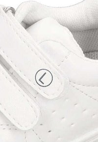 Zapato deportivo blanco con parte superior de cuero liso, correa de gancho y bucle, detalles perforados y un logotipo circular en la correa.