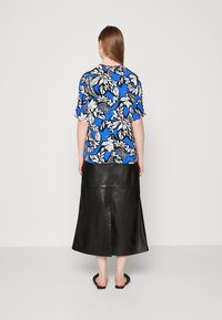 Camiseta con estampado floral en azul, negro y blanco, combinada con una falda larga de cuero negra, que destaca por su textura suave y diseño casual.