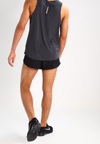 Débardeur de sport pour homme en gris foncé avec une coupe ajustée, accompagné de shorts noirs. Comprend un détail réfléchissant à l'arrière et des chaussures de sport.