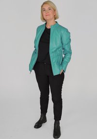Teal nahkalettu, jossa on täyspitkä vetoketju, muotoiltu malli, joustava vyötärö ja mustat housut, jotka on yhdistetty mustiin nilkkasaappaisiin.