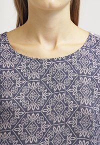 Top navy con un dettagliato motivo floreale bianco con elementi geometrici, scollatura rotonda e una texture di tessuto liscia.