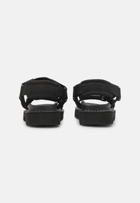 Svarta plattformssandaler med justerbara remmar, med en texturerad sula och vadderat stöd runt ankeln för komfort.