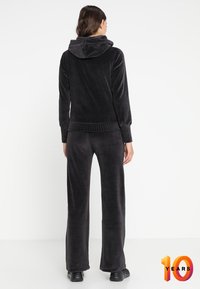 Chándal de terciopelo negro con una parte superior con capucha y pantalones de pierna ancha, con puños y cintura acanalados. Textura suave, diseño minimalista.