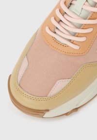 Παπούτσι που συνδυάζει υλικά, συμπεριλαμβανομένου ροδακινί καμβά και ανοιχτό μπεζ δέρμα. Στρογγυλεμένο σχήμα με επίπεδες κορδόνια και υφή στην σόλα.