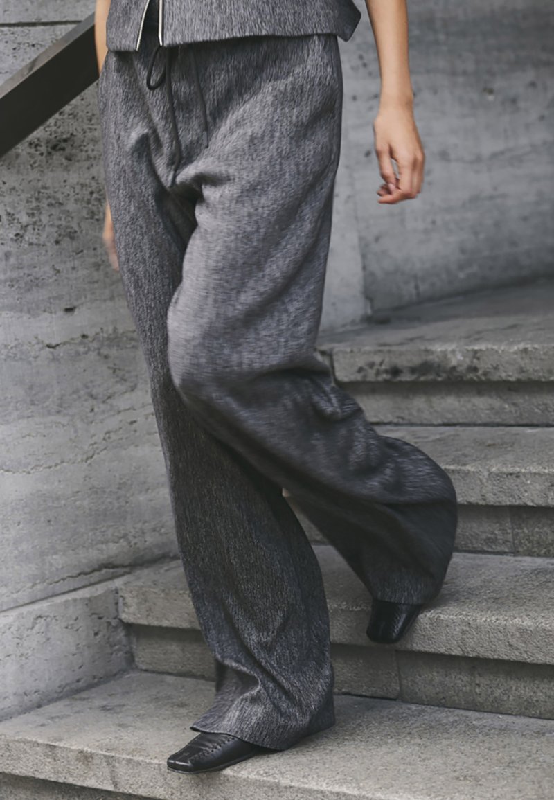 Brede broek in donkergrijze stof met een gestructureerde afwerking. De pantalon heeft een elastische tailleband en past goed bij stijlvolle zwarte schoenen.