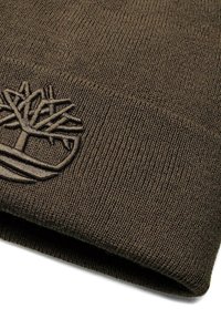 Beanie lavorato a maglia di colore verde oliva, realizzato in tessuto testurizzato, con un logo ad albero ricamato in evidenza sul davanti. Risvolto in basso.