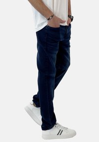 Jeans de mezclilla azul oscuro con un ajuste relajado, que cuentan con bolsillos frontales y un ligero desgastado. Combinados con zapatillas blancas con rayas negras.
