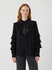 Sort bluse med rysjekrave og plisserte, lagdelte ermer. Laget av glatt stoff med sløyfe i halsen og knappelukking foran.