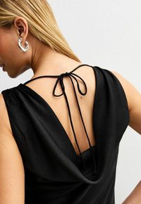 Top senza maniche nero con schiena drappeggiata, chiusura con lacci regolabile e una texture liscia e opaca. Profondo scollo audace che rivela la pelle.