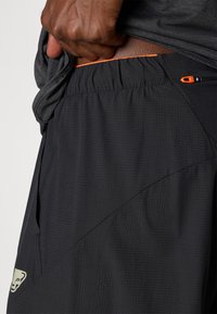 Μαύροι αθλητικοί σορτς με αναπνεύσιμο ύφασμα, ελαστική ζώνη, πορτοκαλί λεπτομ έρειες, υφή και τσέπη με φερμουάρ στο πλάι.