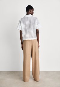 Cropped white patterned shirt with short sleeves, back visible. Paired with tan wide-leg trousers, smooth fabric and relaxed fit.