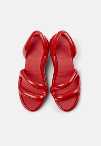 Red molded sandals featuring two overlapping straps and a textured footbed. The glossy finish highlights the shoe's flowing design.